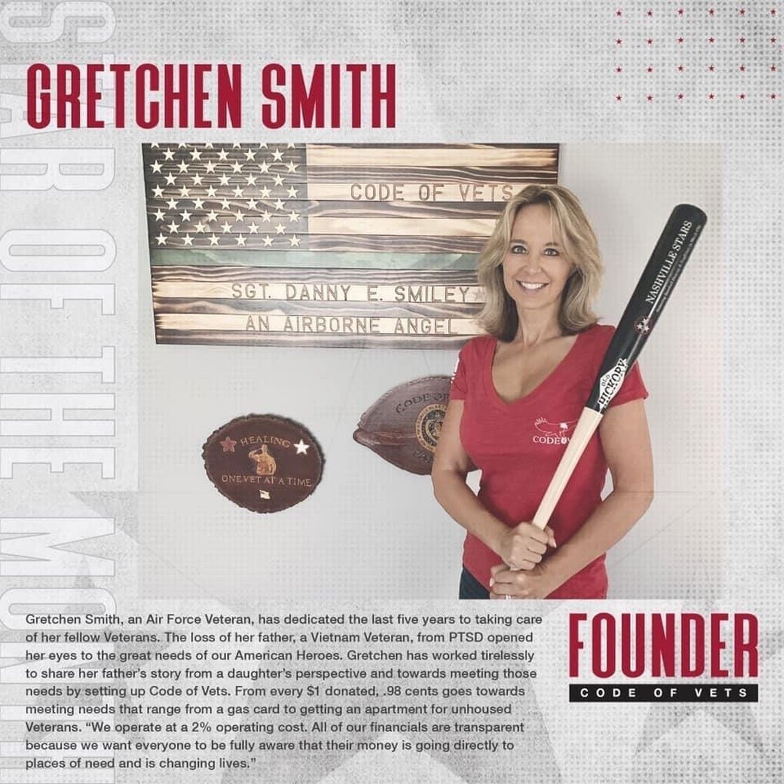 Gretchen Smith, founder of Code of Vets, holding a Nashville Stars baseball bat in front of a wooden American flag honoring Sgt. Danny E. Smiley